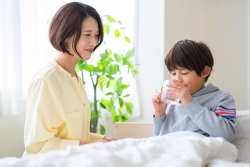 Mother caring for a child drinking water in bed while recovering from a fever.